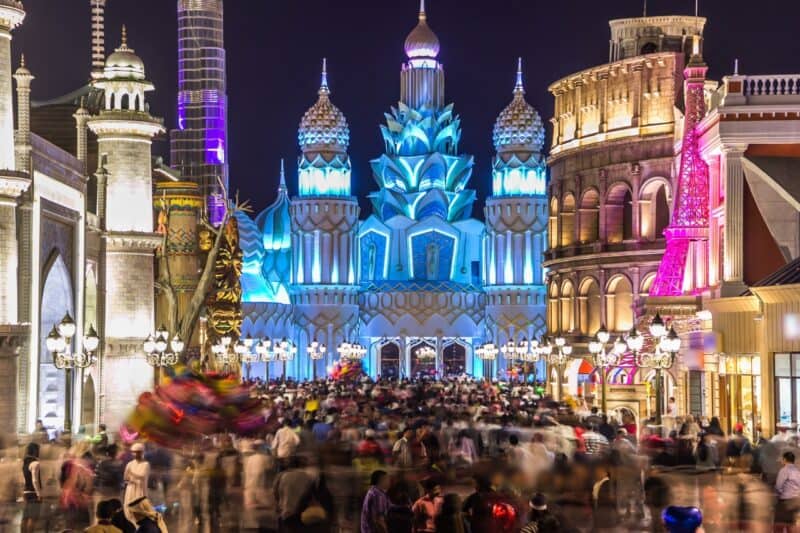 The entrance to Global village lit up at night and a crowd of people passing though