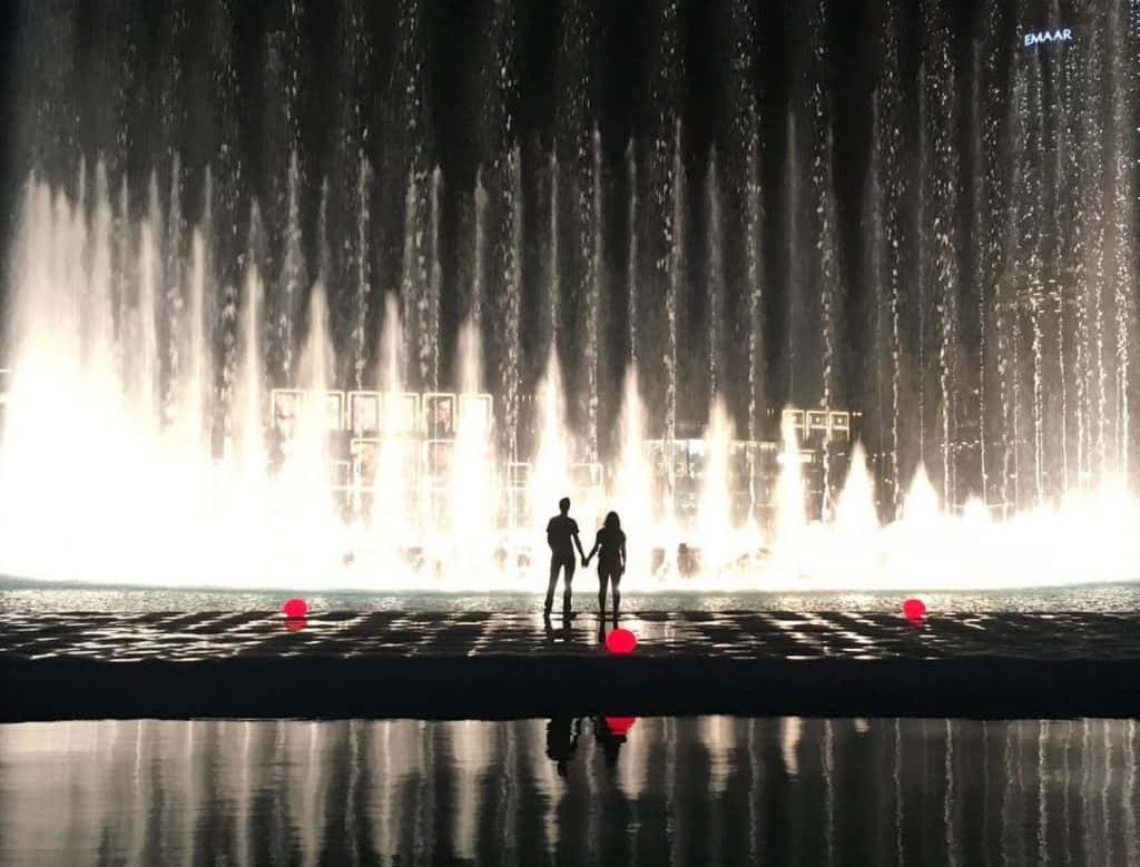 Couple standing watching Dubai Fountain lit up at night at the Dubai Fountain boardwalk