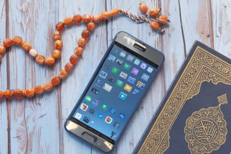 Phone with apps for Muslim prayer reminders at work with a copy of a quran and prayer beads