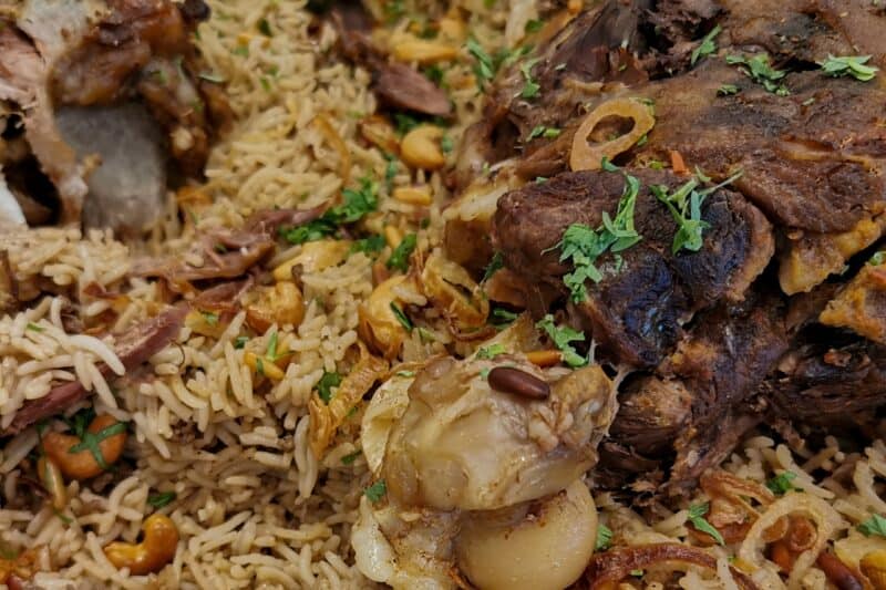 Close up picture of lamb ouzi sprinkled with pine nuts, cashews and fresh herbs