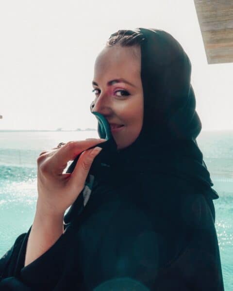 Photo of Danni from Danni in The Desert wearing a traditional Emirati black abaya, standing at the infimity pool of the Mandarin Oriental Dubai hotel in Jumeirah