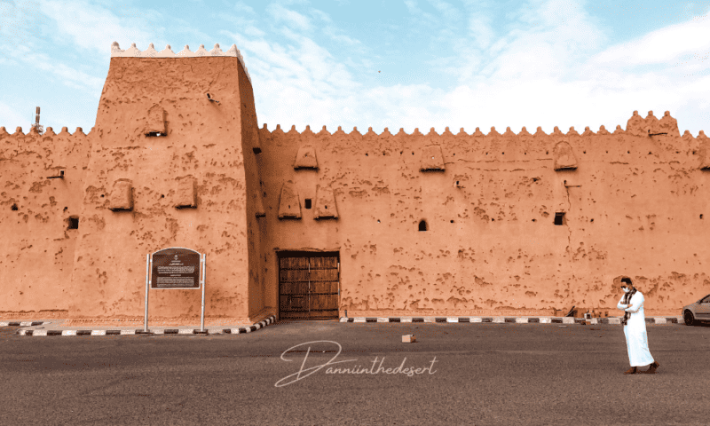 Outside of the Qishlah Palace with parking and a wooden gated entrance, showing traditional Saudi architecture