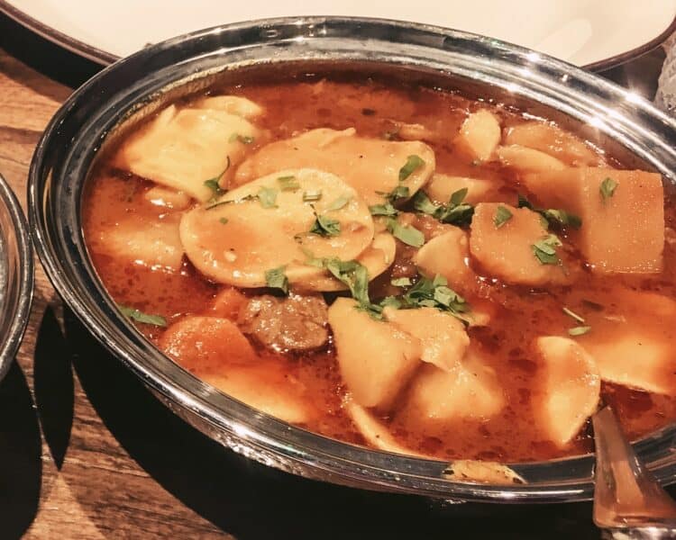 A silver bowl of chicken thareed, also called saloona with sliced potatoes in a tomato based sauce with vegetables