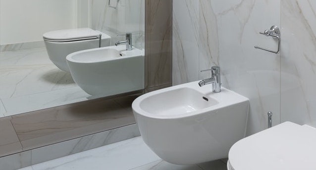 western style white ceramic bidet with silver tap in a bathroom with marble tiles