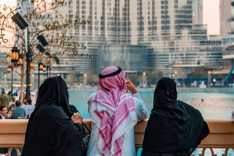 Two women and a man in traditional Khaleeji clothing looking over Dubai Fountain
