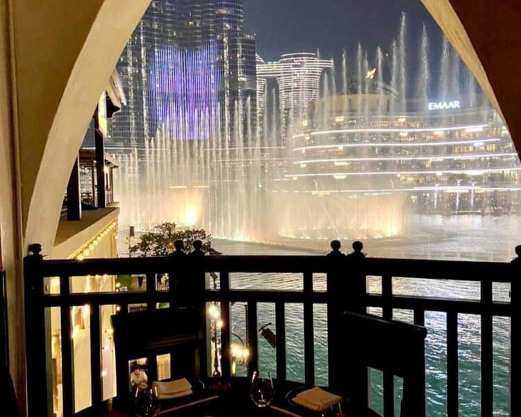 Dubai Fountain lit up with shooting water jets and the Burj Khalifa in the background at the outdoor terrace area at Karma Kafe in Souk Al Bahar