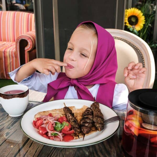 Little girl dressed as Masha enjoying kebab with bread and tomatoes, sat at the table of Masha and The Bear restaurant in Dubai