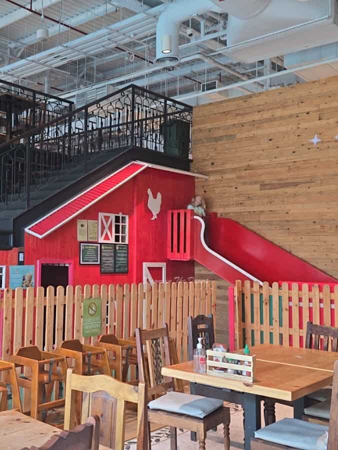 Wooden children's play area in the style of a red wooden chicken coup with a slide close to the eating area in the Organic Foods & Cafe Cityland Mall branch