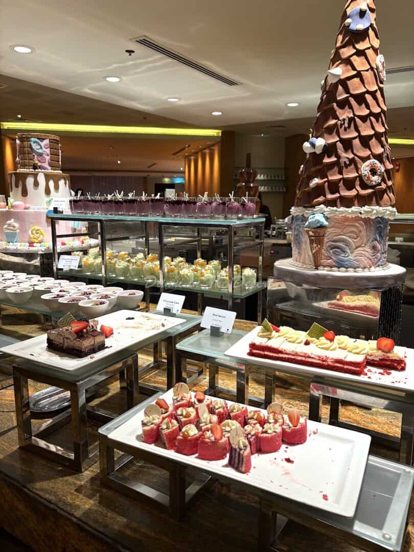 The incredible dessert counter at Kitchen 6's buffet with a chocolate fountain visible at the back, chocolate-decorated display trees, plates of desserts, cakes and little pots of pudding along with another large display cake prettily decorated