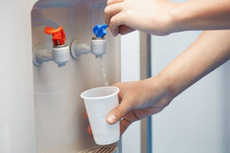 Two hands helping themselves to water from a water cooler with a plastic tap. Water coolers are popular in Dubai and offers refreshing cold water in the hot heat.