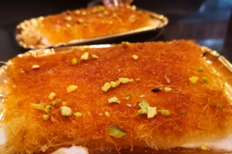 Large portion of kunafa in dubai served on a gold paper tray with sugar syruo and nut pieces