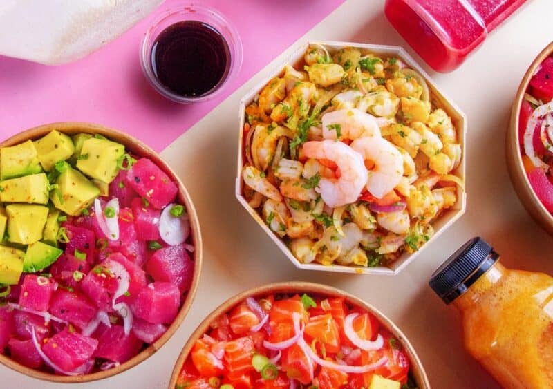 Different cali poke bowls and juices laid decoratively on a table with a pink background