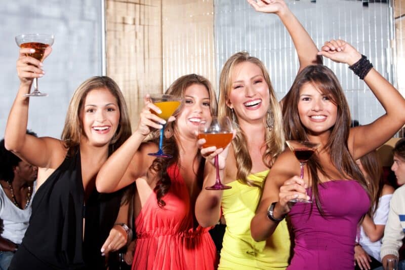 Four women with cocktails in their hands enjoying a Dubai Brunch and wearing cocktail dresses.