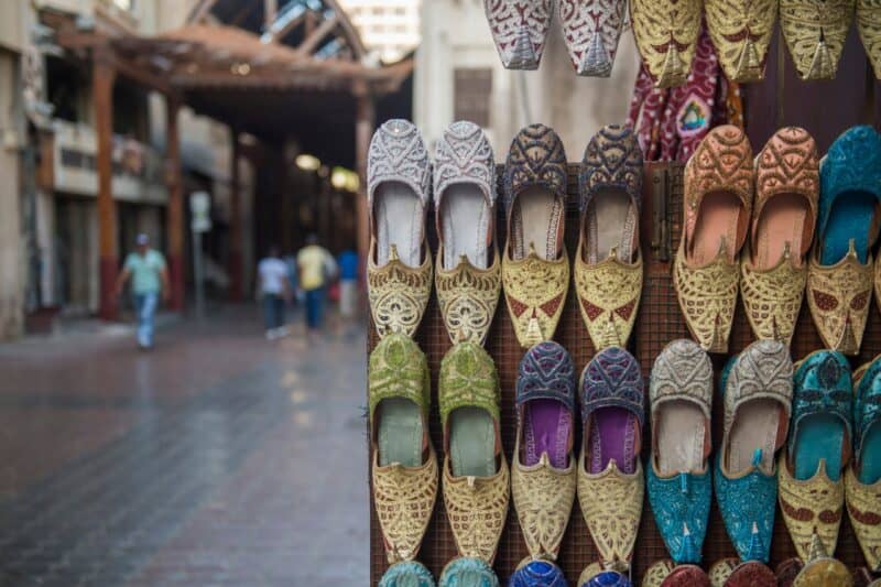 Unique hand made shoes stacked in a shop display wall with Dubai Souq in the background