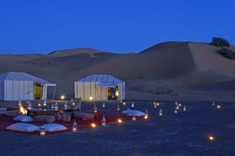 Tents set up in the desert with candlelight and bedouin style cushions with carpets ready for a dinner