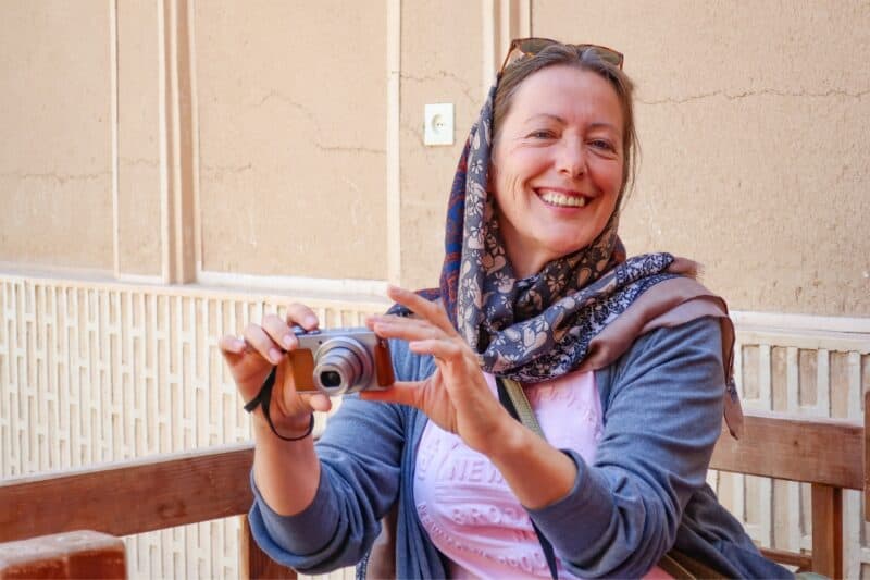 An older female tourist wearing a hijab or scarf over her hair while taking a photo in Dubai.