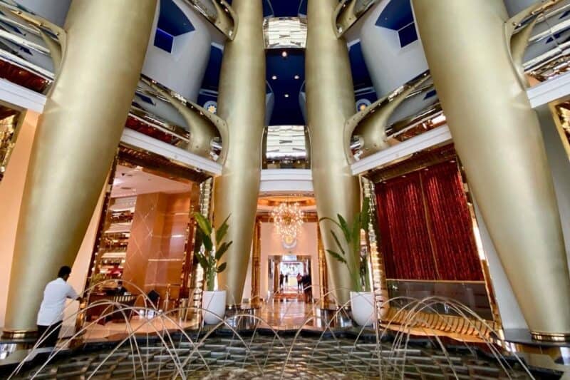 Inside the lobby of Burj Al Arab with the geometric patterned water fountain and columns covered in real gold leaf, leading towards the lifts at the back towards the restaurants