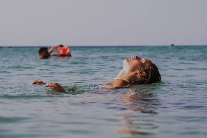 A woman lying back in the sea, while a man and a child swim in the background in the sea at a beach in Dubai