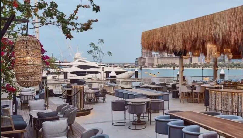 Outdoor terrace and seating of Bar Du Port Dubai with a super yacht in the background