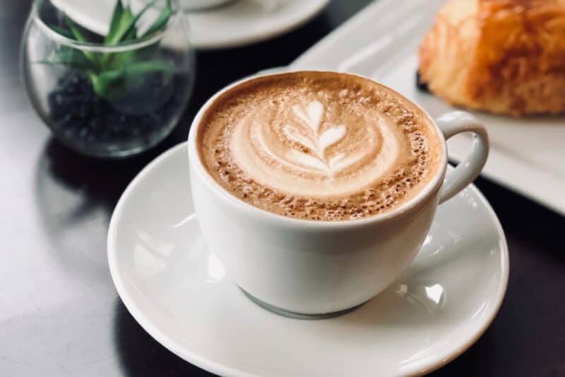 large coffee in dubai with a pastry on a table in a cafe with a small plant in a small glass bowl