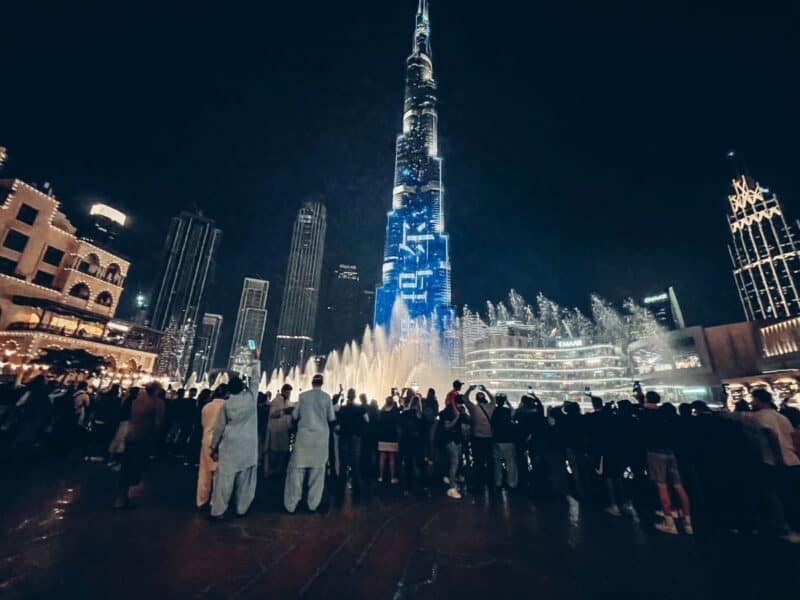 People watching the Dubai Fountain at night, with the Burj Khalifa building lit up, which is connected to the Burj Khalifa's sewage system