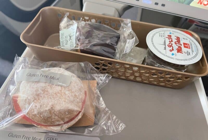 An Emirates airline meal gluten free snack sandwich with water and a small dessert from Lime Tree Cafe in Dubai on an Emirates airplane tray table A380
