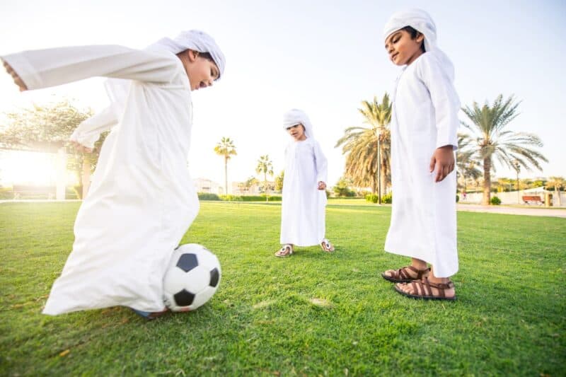 Emirati boys in the park playing football in their traditional Dubai clothes with a kandura and ghutra