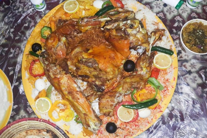 A very large plate of meat machboos placed on a sufra on the floor, ready for people to eat.