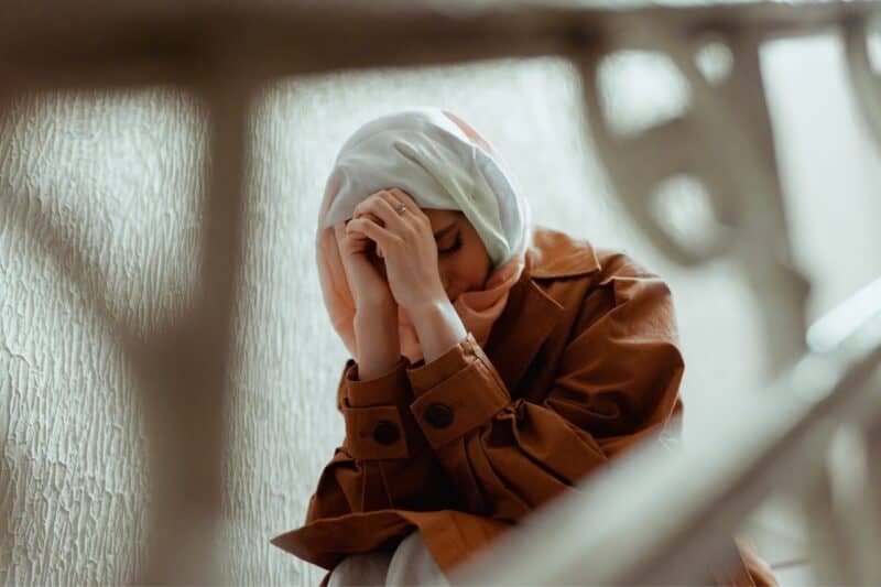 Convert Muslim sat on the stairs looking worried, praying into her hands and facing problems revert muslims face