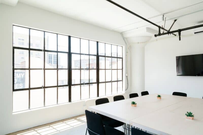 Empty office meeting room, perfect for muslim prayer times, with a white table, black chairs and a tv.