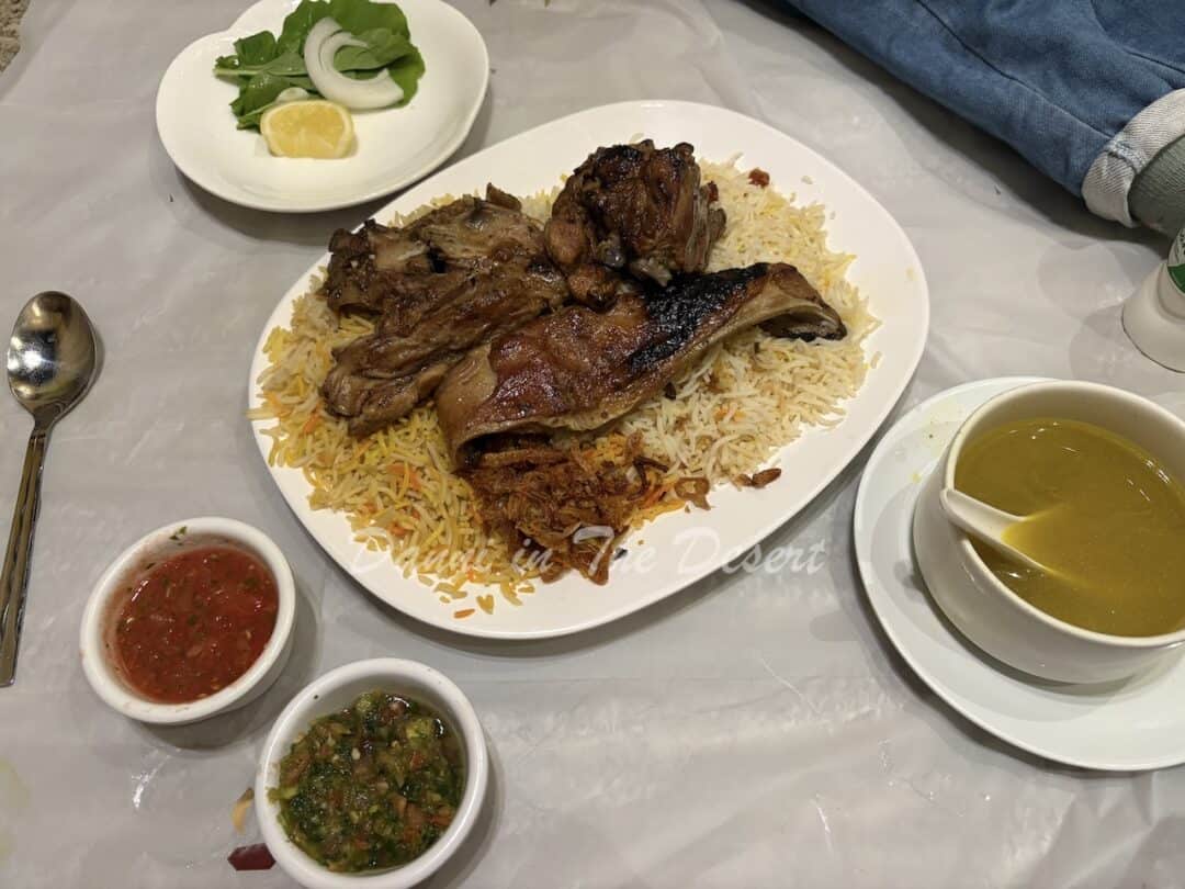 Madhbi meat meal with a soup side, small salad and traditional spicy sauces served on a plastic mat called a sufra