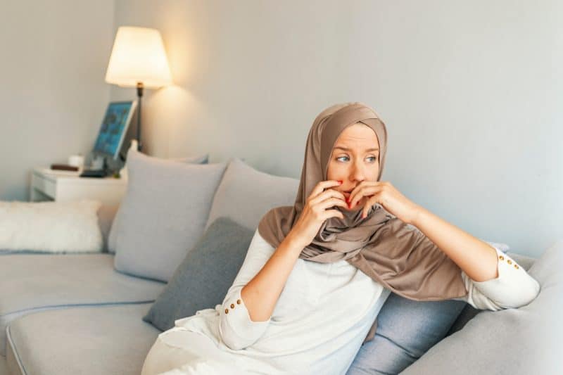 Convert Muslim sitting on a sofa looking overcome with worry. Telling your family you are Muslim can be stressful and difficult but having a good support network can help.