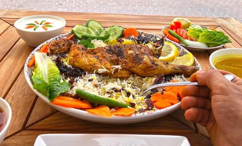 Chicken mandi served with salad and side dishes on a wooden table at Dubai Marina