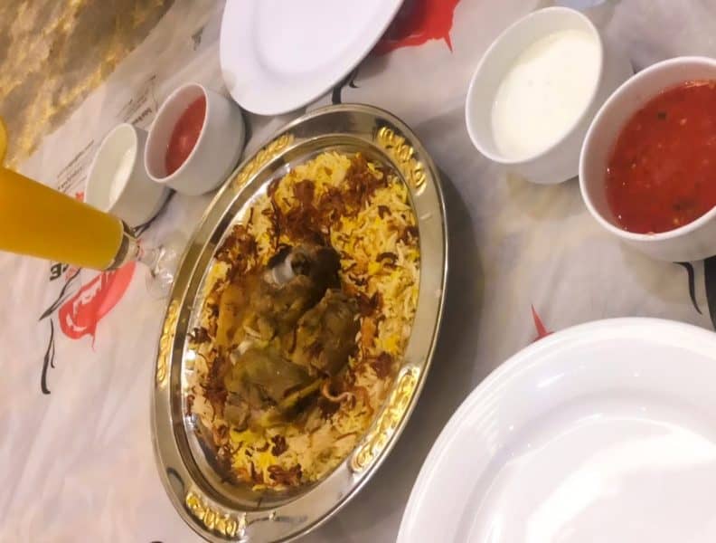 Meat mandi served in a silver, served with yoghurt and red sauce on a plastic sufra.