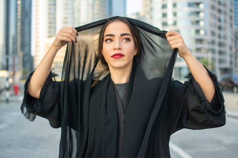 Woman putting on hijab and covering her hair in Dubai wearing an abaya