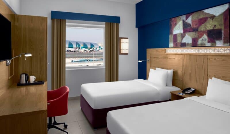 Modern twin hotel room with a desk and window view overlooking Dubai Airport at Holiday Inn Express Dubai Airport