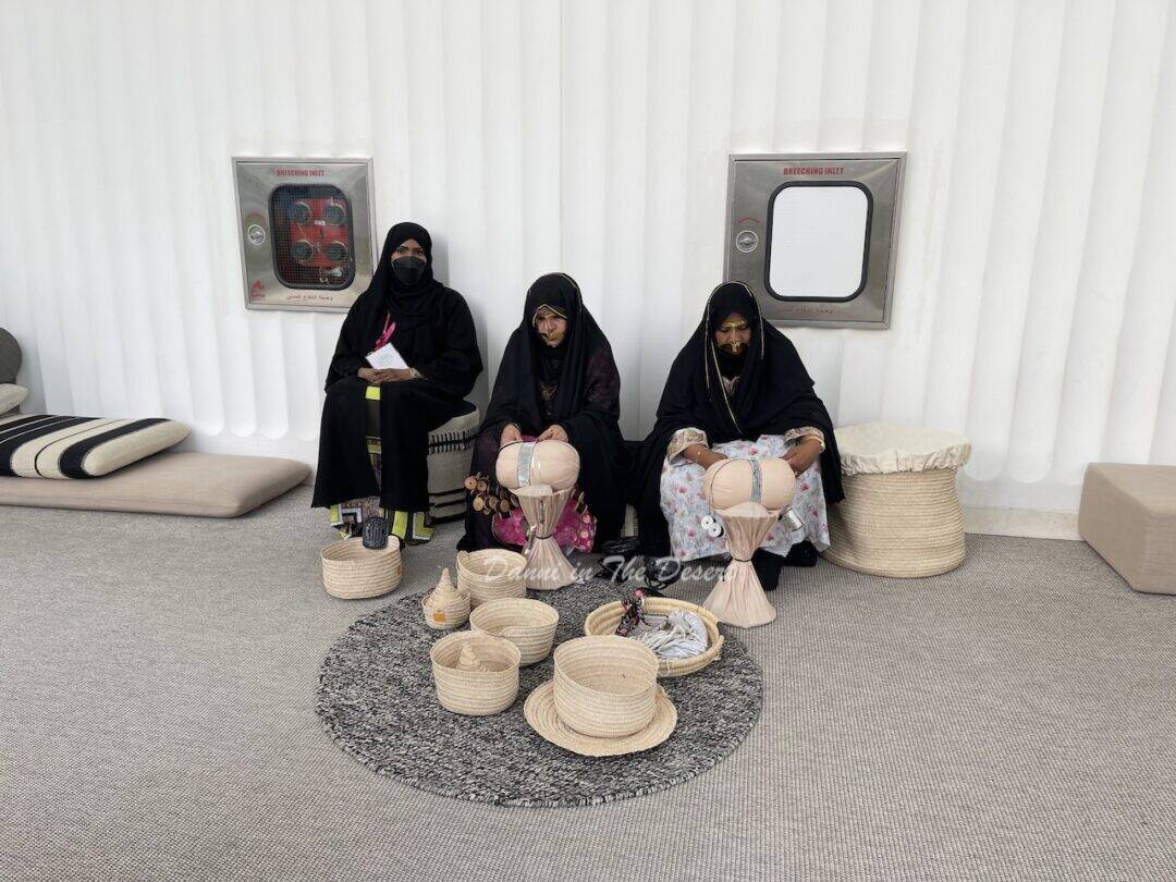 Women wearing traditional Emirati dress including the gold face mask called a burqu or battoulah, making traditional Emirati crafts and weaving 
