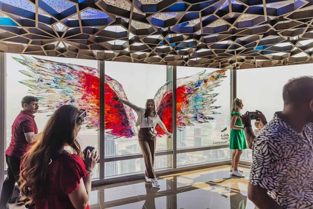 A woman standing in front of the famous colourful wings painted on glass inside the observation deck at Burj Khalifa At The Top with other visitors around her