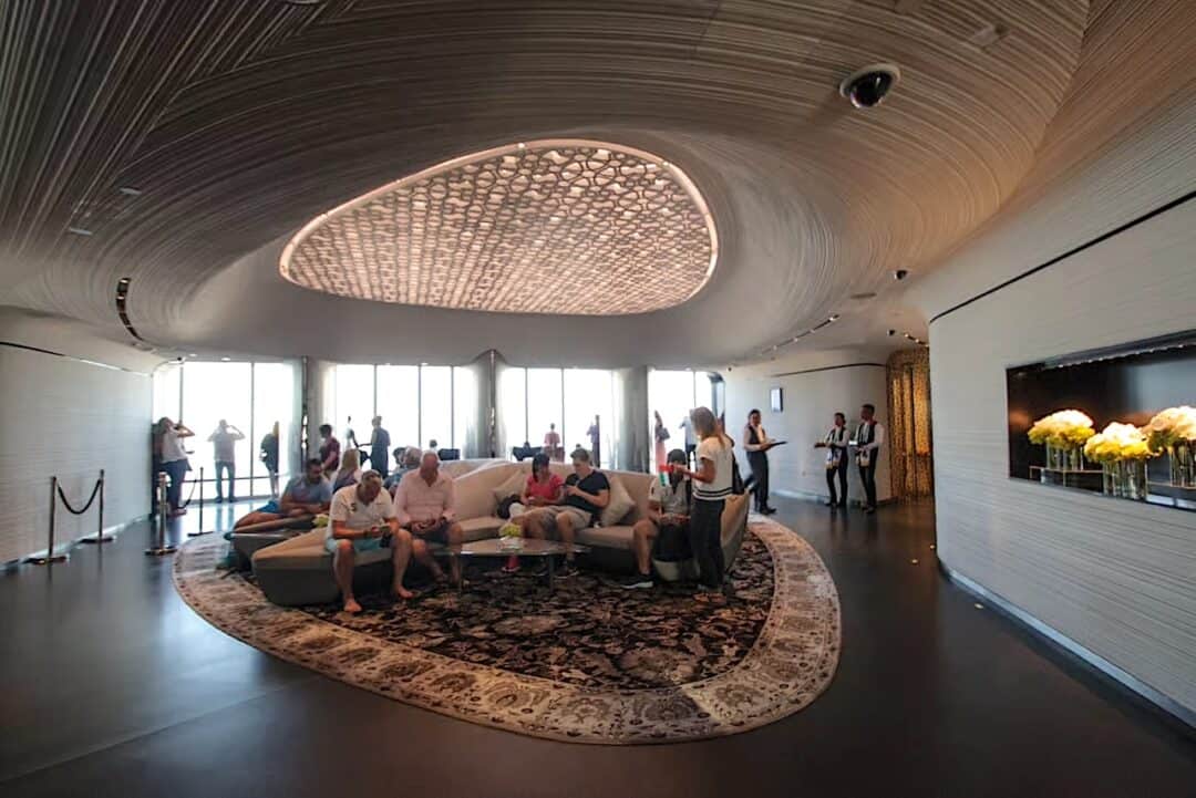 People sat inside the Burj Khalifa Gold Ticket lounge on the 148th floor of At The Top Burj Khalifa with a uniquely shaped rug on the floor and ultra modern decor
