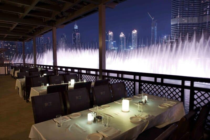 View of the Dubai Fountain lit up and Burj Khalifa, table set up at the outdoor dining area of Thiptara