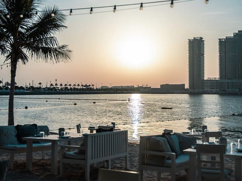 White wooden table and chairs set up close to the sea, sun set on the beach at Fish Beach Taverna in Dubai Marina