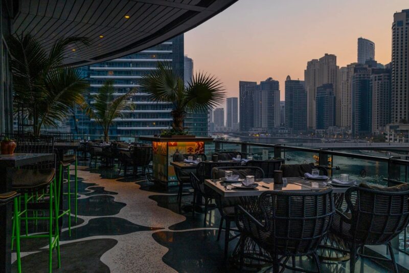 A curved outdoor terrace at Mama Zonia i Pier 7 with the sun setting in the background over Dubai Marina