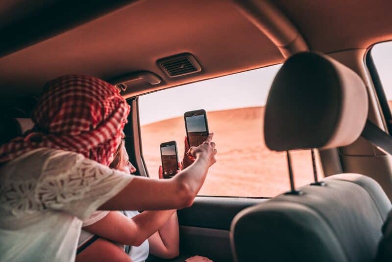 Two women dressed for a desert safari and taking photos of the Dubai desert inside a 4 x 4 car