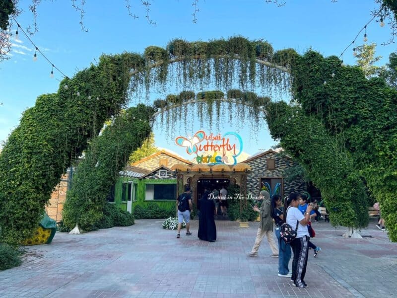 Entrance to the beginning of Dubai Butterfly Garden after the ticket gate with arches made of greenery and the Dubai Butterfly Garden sign