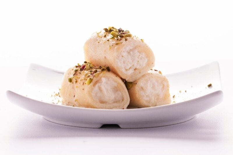 3 pieces of Halawet el jibn served on a  decorative white dish and pistachio with rose sprinkled on top