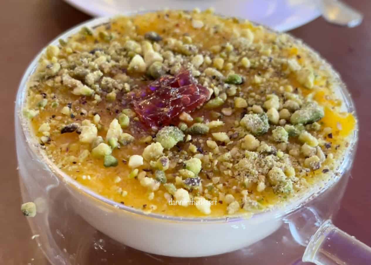 A close up of a mahalabia dessert with nuts and sugar sprinkled on top in a small glass bowl