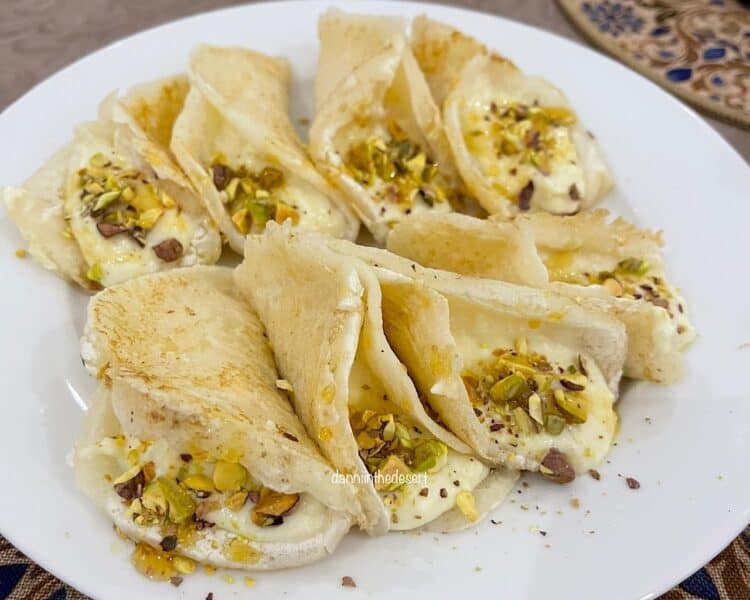 Qatayef filled with a traditional cream called ashta and served with chopped pistachios on a white plate