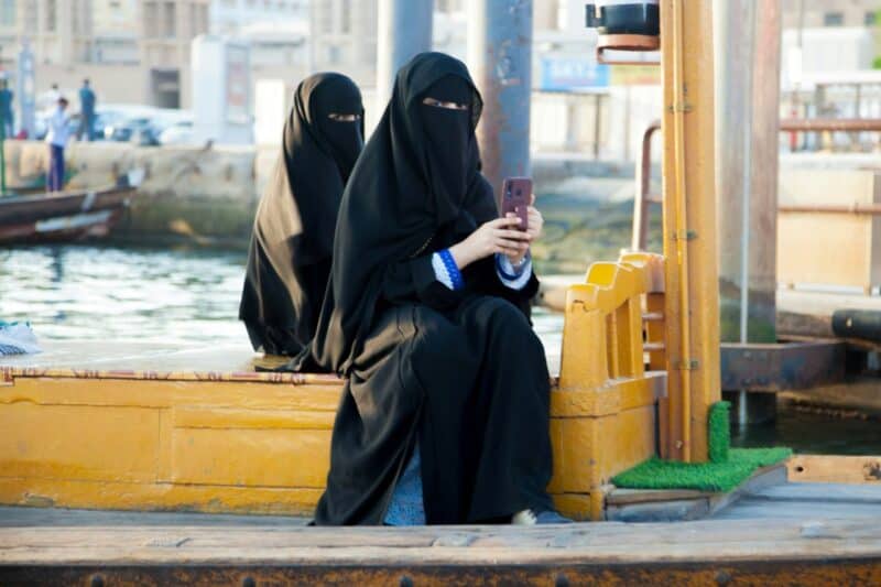 Two women in Niqab taking a photo while someone else takes a photo of them by Dubai Creek