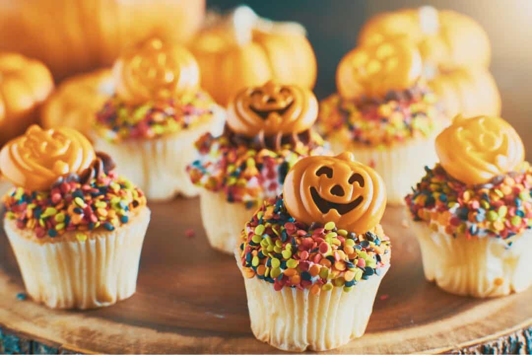 Halloween decorated cupcakes with sprinkles and pumpkins on a wooden chopping board