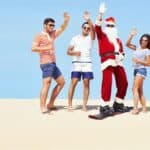 3 people standing on a sand dune in shorts and t-shirts with santa in the middle getting ready to sand board